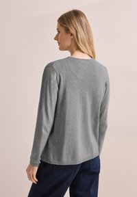 Grauer langärmeliger Pullover mit Rundhalsausschnitt, aus weichem Stoff, mit gerippten Saum- und Bündchendetails, getragen zu marineblauen Hosen.