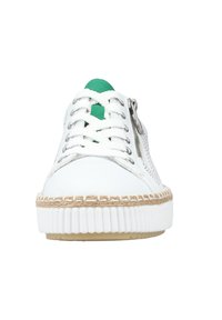 Baskets blanches avec accents verts, côtés en maille textile et semelle en corde tressée. Présente un devant à lacets et un détail de fermeture éclair sur le côté.