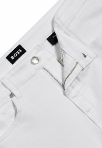 Białe bawełniane spodnie z zamkiem błyskawicznym i zapięciem na guzik, z czarnymi metkami i srebrnymi detalami. Gładka tekstura, dopasowany krój.