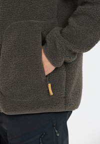 Fleecejacka i mörkgrått med en strukturerad, mjuk yta. Har en ficka med dragkedja och läderdrag, ribbade ärmslut och en avslappnad passform.