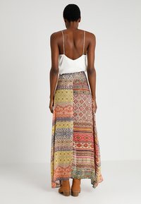 Maxirok met een eclectisch patchworkpatroon in verschillende kleuren, gemaakt van lichtgewicht stof, gecombineerd met een witte satijnen top.