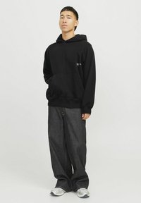 Haut à capuche en coton noir avec une poche avant et des poignets côtelés, associé à un jean en denim foncé à coupe ample et des baskets argentées.