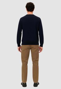 Suéter de punto azul marino con cuello redondo, combinado con chinos color beige. El conjunto presenta un diseño ajustado y una textura suave.