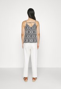 Caraco à motifs noir et blanc avec fines bretelles, présentant un dos en V, porté avec un pantalon large écru et des sandales marron clair.