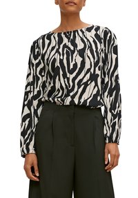 Femme portant un chemisier à motifs abstraits noir et blanc à manches longues, rentré dans un pantalon noir large à taille haute.