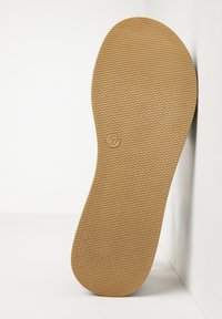 Sól hnědé gumové boty s texturovaným šestiúhelníkovým vzorem a označením velikosti 37, opřená o bílou zeď na bílé ploše.