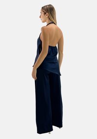 Navy satijnen haltertop met een open rug, gecombineerd met brede navy broek. Gladde textuur, vloeiende ontwerp, minimalistische silhouet.