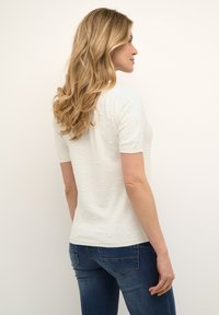 Hvid strikket kortærmet sweater med teksturerede polka dots. Blødt materiale med en tætsiddende form. Bæres med mørkeblå jeans.