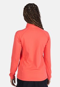 Långärmad topp med zip-hals i klar korall, tillverkad av slät och elastisk tyg. Har raglanärmar och platta sömmar för ökad komfort.