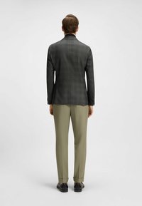 Czarna marynarka w kratę o dopasowanym kroju, z czarnym kołnierzem, połączona z jasnooliwkowymi spodniami. Gładka tekstura, bez widocznych wzorów, z subtelnymi akcentami.