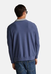 Jasnoniebieski sweter z szarym kołnierzem, z prążkowanym dołem i mankietami. Noszony z niebieskimi dżinsami, widok z tyłu.