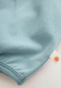 Tissu bleu clair doux avec bord côtelé et petite étiquette beige comportant un motif circulaire orange, attachée à la couture.