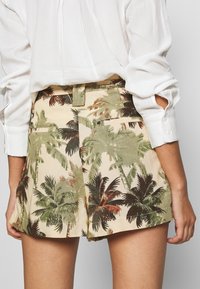 Pantalones cortos marrones con un estampado de palmeras verdes y marrones, de cintura alta, con bolsillos laterales y un diseño de pierna ancha.