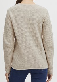 Beżowy sweter dziany o fakturowanej powierzchni, z długimi rękawami i ściągaczami przy mankietach. Posiada okrągły dekolt oraz lekko zaokrąglony dół.