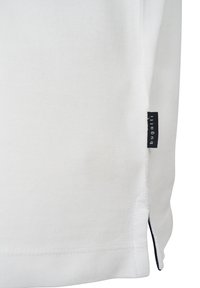 White polo shirt featuring textured fabric, side vent with contrasting navy trim, and a small black brand tag at the hem.