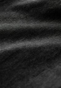 Tessuto nero con una superficie liscia e texture. Leggeri riflessi evidenziano i motivi intrecciati e le morbide pieghe presenti nel materiale.