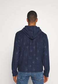 Felpa con cappuccio di colore blu navy con un motivo a diamante testurizzato. Presenta una vestibilità comoda e polsini a coste. Tessuto liscio di media densità.