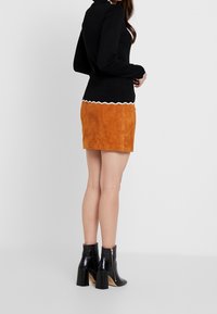 Svart långärmad topp med vågig vit nederkant, kombinerad med en orange mocka minikjol och svarta klackade ankelstövlar med dragkedja på sidan.