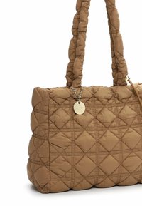 Quilted brown handbag with padded handles and a small round gold tag hanging from one handle, set against a white background.
