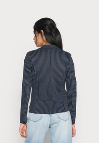 Tummansininen pinstripe-takki, jossa pitkät hihat, muotoiltu istuvuus, yksinkertainen takaselkäventti ja lovet lapelit, yhdistettynä vaaleansinisiin korkeavyötäröisiin farkkuihin.
