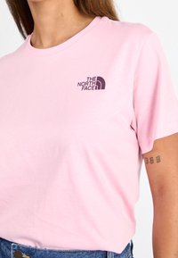 T-shirt di cotone rosa con scollatura rotonda, che presenta un logo viola scuro "The North Face" sul lato sinistro del petto e maniche corte.