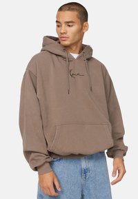 Bruine hoodie van zachte stof, met een voorzak, een capuchon met trekkoord en een zwart script logo op de borst. Relaxed fit met geribbelde manchetten.