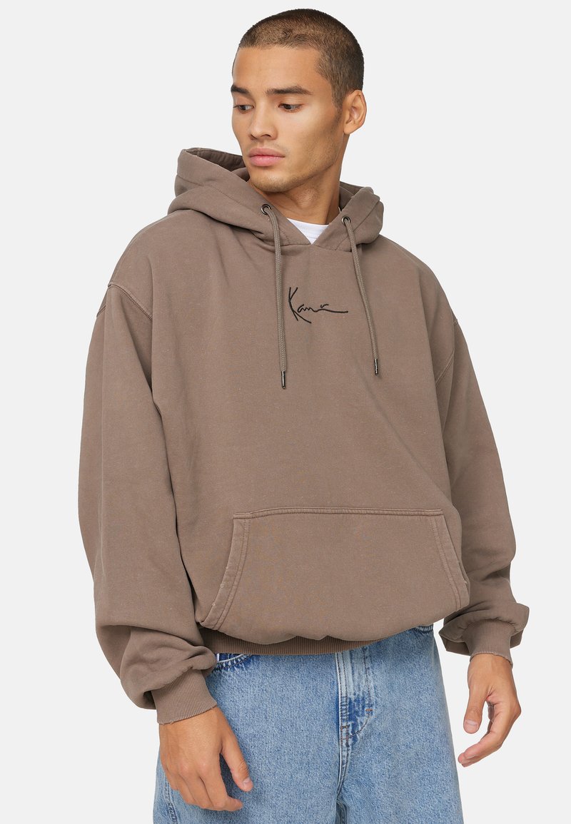 Bruine hoodie van zachte stof, met een voorzak, een capuchon met trekkoord en een zwart script logo op de borst. Relaxed fit met geribbelde manchetten.
