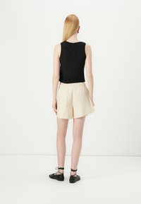 Svart ermeløs topp kombinert med kremfargede shorts, med elastisk midje, lett design og svarte snøring-lettvektsko. Glatt tekstur.