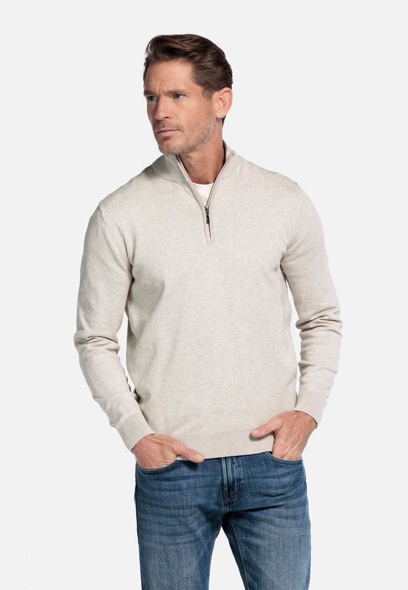 Lichtgrijze pullovertrui met een rits-halflange kraag, geribbelde manchetten en zoom, gedragen over een wit shirt, in combinatie met blauwe jeans.