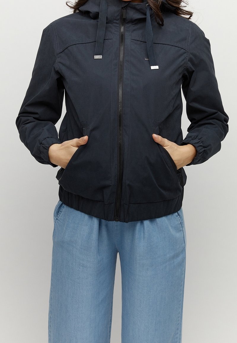 Granatowa kurtka przeciwwiatrowa z zamkiem z przodu, regulowanym kapturem, elastycznymi mankietami oraz bocznymi kieszeniami. Gładki materiał z dopasowaną talią.