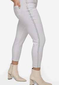 Hvide fitted jeans med en sidepynte af metalliske perler og mønstre, med lommer og cropped kant, parret med beige ankelstøvler.