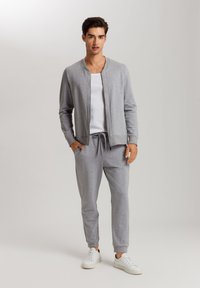 Giacca sportiva grigia con orlo e polsini a costine, abbinata a pantaloni della tuta con coulisse e sneakers bianche. Tessuto di superficie liscia.