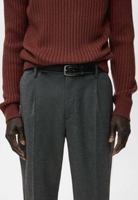Prążkowany bordowy sweter połączony z szarymi dopasowanymi spodniami, z czarnym paskiem. Materiał spodni wydaje się mieć teksturę i charakter formalny.