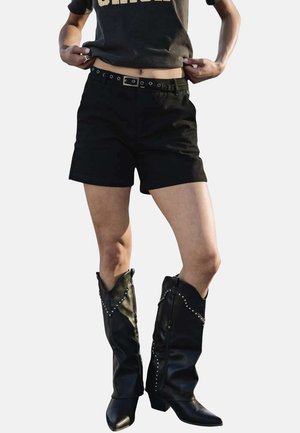 Sorte bomuldsbukser med slim fit, ledsaget af sort læderstøvler til knæene, der har sølvnitter og spidse tår.