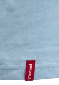 Ljusblå bomulls-T-shirt med en röd tygetikett med "hummel" text längst ner, synlig sömnad längs fållen.