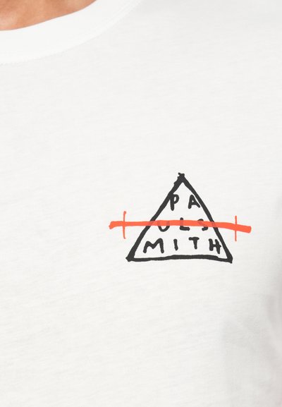 Valkoinen puuvillapaita, jossa on musta ja oranssi kolmiomainen graafinen kuva, jossa teksti "PAUL SMITH" on yliviivattu. Yksinkertainen, minimalistinen muotoilu.