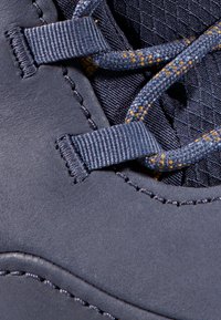 Scarpa blu scuro in pelle liscia con rivestimento interno testurizzato. Include lacci grigi con accenti gialli e dettagli di cucitura rinforzata.