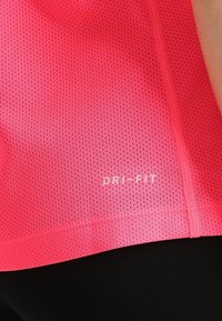 Primo piano di una maglietta sportiva rosa perforata con il logo "DRI-FIT" sopra leggings neri.