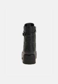 Stivale alla caviglia nero con motivo a rilievo, dotato di zip laterale, cinturino regolabile e suola nera spessa. Nome del marchio impresso sul tallone.