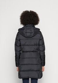 Abrigo acolchado negro con capucha, textura acolchada y puños elásticos, que llega hasta la mitad del muslo con un corte recto.