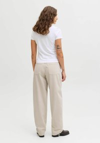 T-shirt blanc à manches courtes associé à un pantalon beige clair à jambes larges. Le pantalon dispose de poches arrière et d'une coupe décontractée. Bottines noires.