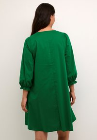 Grön bomullsklänning med puffärmar, rundad halsringning och rak passform. En söm går längs mitt bak för extra detalj.