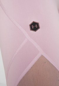 Ljust rosa träningsleggings med en hexagonal svart logotyp, featuring meshpaneler och platta sömmar för ökad komfort och passform.