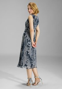 Vestido de estampado floral en azul y gris, con un corsé ajustado y una falda acampanada, complementado con tacones plateados con tiras.