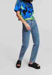 Grafický crop top v modré a zelené barvě, spárovaný se světle modrými džíny. Model má na sobě černé platformové sandály. Uvolněný střih.