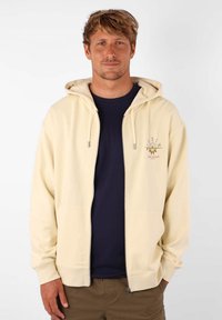 Hoodie zippé jaune clair avec une poche avant et une capuche à cordon. Présente un motif imprimé sur la poitrine et des poignets côtelés.