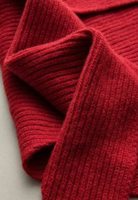 Tissu tricoté rouge drapé, mettant en valeur une texture côtelée. Le matériau semble doux et épais, avec une profondeur variée dans les côtes.