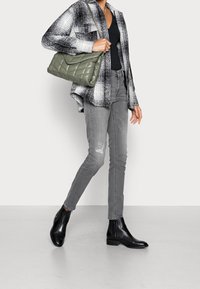 Černobílé kostkované tričko přes černý top, šedé skinny džíny s dírou, černé kotníkové boty a zelená prošívaná kabelka.