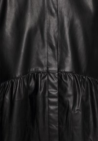 Svart läderplagg med en samlad textur i den nedre delen, slät yta och sömdetaljer.