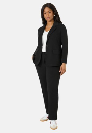 Blazer noir avec revers crantés et deux poches avant, associé à un pantalon noir et un t-shirt blanc. Terminé avec des baskets blanches.